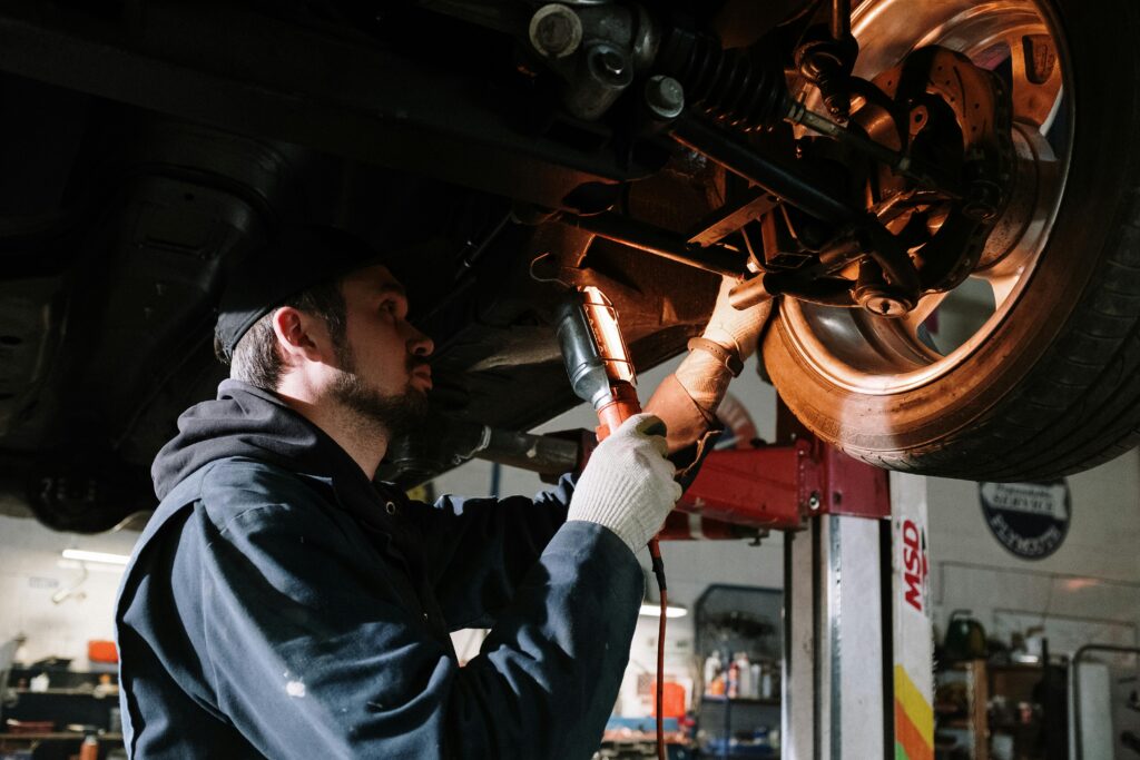 pexels-photo-4489749-4489749 Mechanic examining car's undercarriage at a garage, focusing on vehicle maintenance.